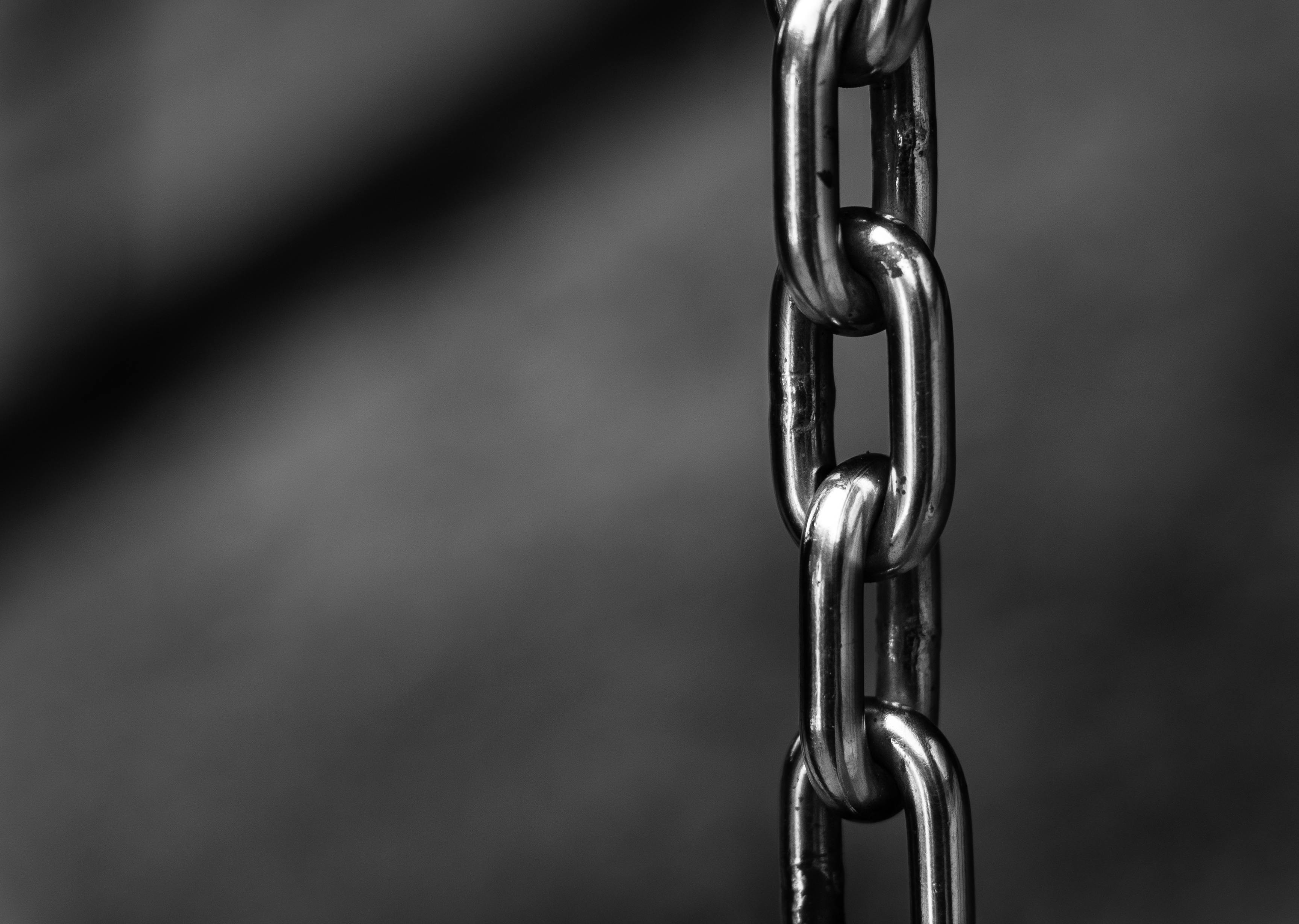 Close-up of a vertical metal chain in grayscale, with a soft-focus background. The chain links are shiny and smooth, conveying strength and connection.